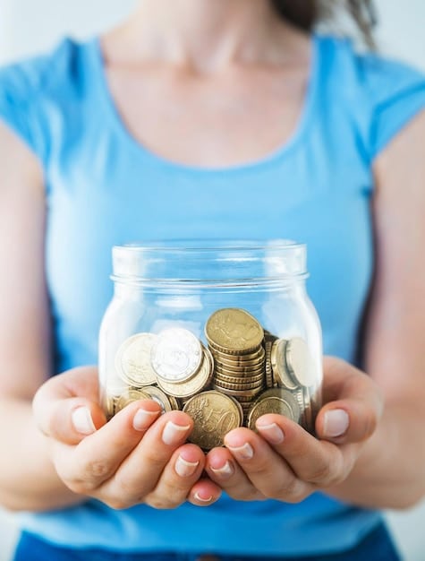 A hand inserting coins into a clear glass jar labeled 