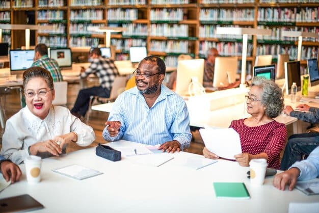 A diverse group of teachers sitting around a table in a school lounge, smiling and engaging in a lively discussion. The room features colorful posters and decorations, and the scene conveys a sense of camaraderie and shared commitment to education.