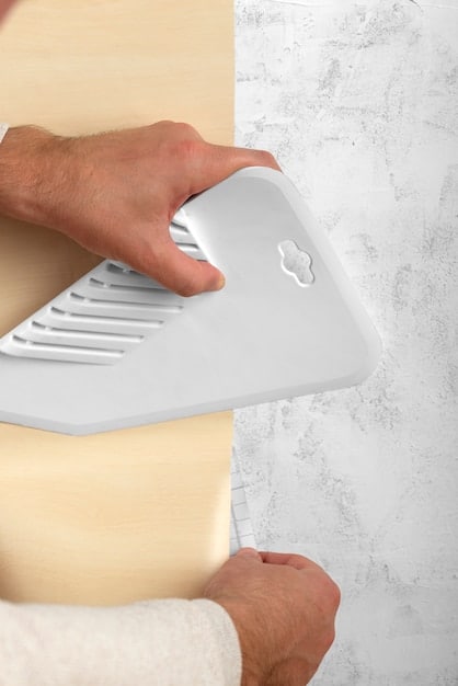 Close-up shot of a person's hands carefully sanding a kitchen cabinet door with sandpaper. Dust particles are visible in the air, indicating the sanding process. The cabinet door is partially painted in a light gray color, showing the transition from the original finish.