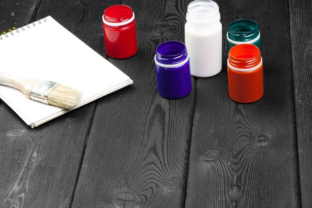 Assortment of painting supplies laid out on a protected surface, including paint cans, primer, paint brushes, rollers, sandpaper, painter's tape, and drop cloths. The color palette is neutral, with shades of white, gray, and beige dominating the scene.