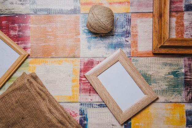 A close-up shot of a variety of thrifted frames arranged on a wooden table. The frames include different materials like wood, metal, and plastic, and various styles like ornate, vintage, and modern. Each frame contains either a piece of artwork or a blank canvas, showcasing their potential for a gallery wall.