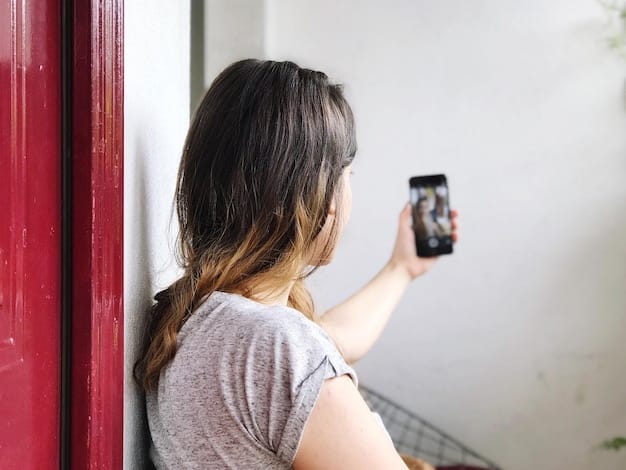 Close-up of a person using a smartphone to view the live feed from their DIY smart doorbell. The phone screen shows a clear image of a visitor standing at the front door.